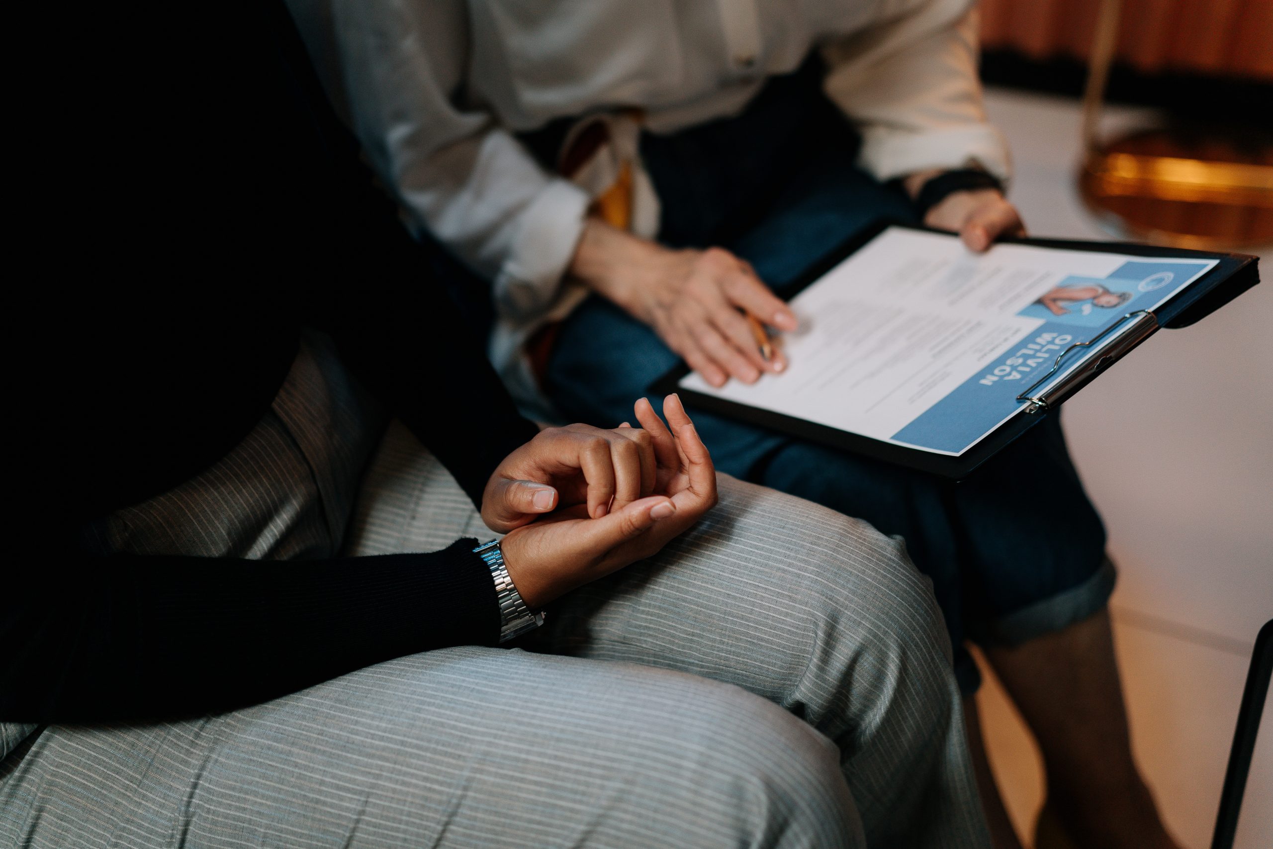 Two people are sitting. One person holds a resume.
